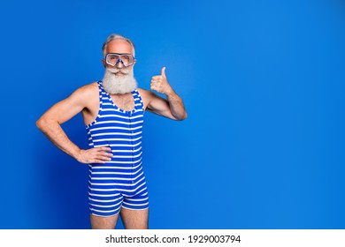 Photo of happy positive good mood old man in swimming goggles showing thumb-up isolated on blue color background
