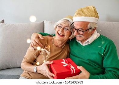 Photo of Happy senior couple exchanging Christmas presents during the day at home. Elderly woman giving present to her beloved husband. Gray hair couple celebrating New Year - Powered by Shutterstock