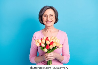 Photo of happy smiling good mood pretty mature woman in glasses hold bouquet of tulips isolated on blue color background