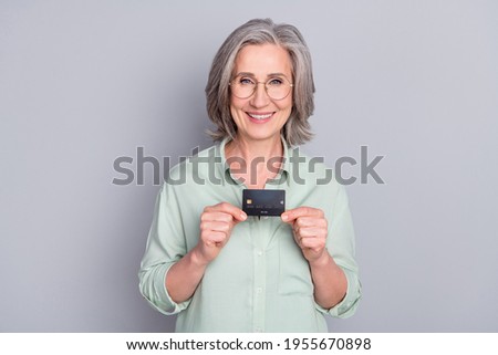 Photo of happy smiling lovely sweet grandma in glasses hold credit card isolated on grey color background