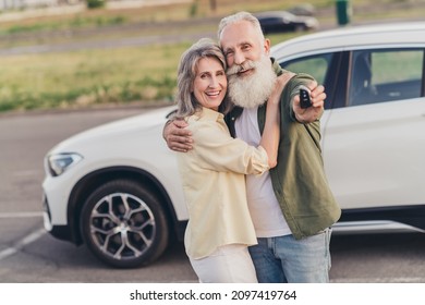 Photo of happy wife husband old people new car keys hug enjoy good mood smile parking outside outdoors in city