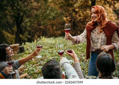 A photo of a happy woman with a wineglass giving a welcome speech at the table. A young female is looking at friends. They are socializing in restaurants' open space outdoors. - Powered by Shutterstock