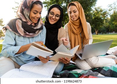 Photo of a happy young arabian women students using laptop computer and holding books in park. - Powered by Shutterstock