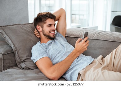 Photo Of Happy Young Man Lies On Sofa And Looking On Phone