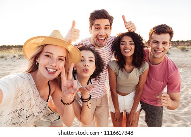 Photo of happy young multiracial people in summer clothes taking selfie while standing at the beach during sunset - Powered by Shutterstock