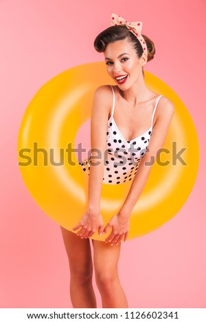 Photo of happy young pin-up woman isolated over pink background wall in swimwear with inflatable ring.