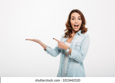 Photo of happy young woman standing isolated over white wall background. Looking camera showing copyspace pointing. - Shutterstock ID 1013442520