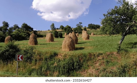 Photo of hay sheaves on a green hill under the clouds - Shutterstock ID 2332616427