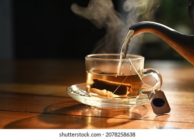 photo of hot water pouring into transparent cup with tea bag inside on wood table in morning sunlight - Powered by Shutterstock