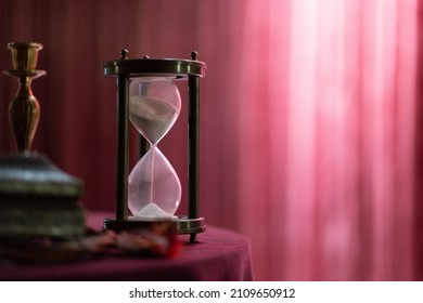 Photo of an hourglass on a table against the backdrop of a red curtain. Interior and time concept. - Powered by Shutterstock