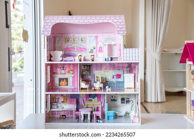 The photo of huge pink dollhouse model furnished with miniature furniture in a kid’s room. 