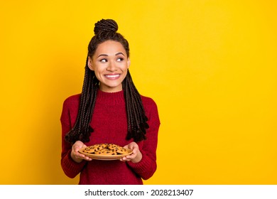 Photo Of Hungry Shiny Dark Skin Woman Dressed Sweater Holding Plate Cookies Looking Empty Space Smiling Isolated Yellow Color Background