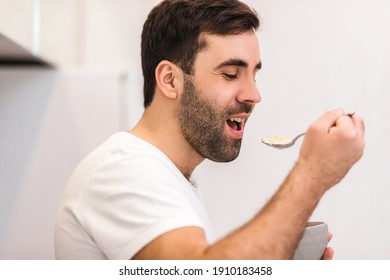Photo of hungry young man eating breakfast from bowl.