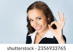 Photo image of businesswoman in confident black suit showing ok okay gesture, isolated blue color background. Executive employee, bank manager, business woman - studio ad concept.