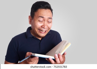 Photo Image Of Cute Funny Asian Man Crying While Reading Book On His Hand