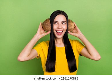 Photo of impressed dreamy lady dressed yellow t-shirt holding two coconut slices empty space isolated green color background