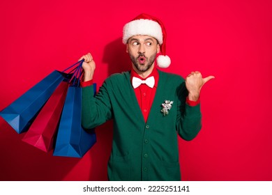 Photo of impressed funky guy dressed xmas green cardigan bowtie buying noel gifts shoppers thumb empty space isolated red color background - Shutterstock ID 2225251141
