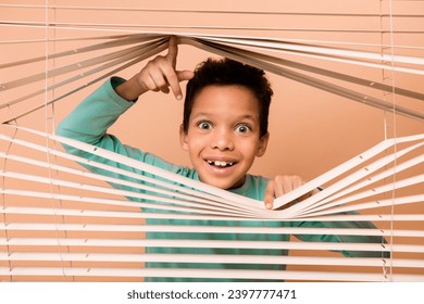 Photo of impressed funky small person open look interested through window shutter curtain isolated on beige color background
