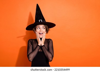 Photo of impressed funny lady wear black witch dress cap arms hands cheekbones cheeks looking empty space isolated orange color background