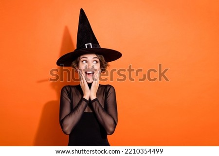 Photo of impressed funny lady wear black witch dress cap arms hands cheekbones cheeks looking empty space isolated orange color background