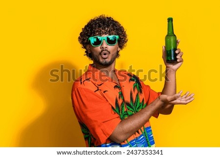 Photo of impressed man with afro hairdo dressed print shirt in sunglass demonstrate beer in arm isolated on yellow color background