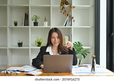 Photo Of An Insurance Agent Working At The Wooden Working Desk Surrounded By A Computer Laptop, Document, Clipboard, Calculator And Various Office Equipment.