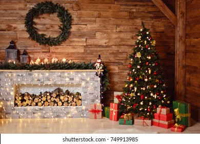 Photo of interior of room with a wooden wall, wreath and garlands, Christmas tree, fireplace with firewood. Christmas atmosphere. Home comfort
