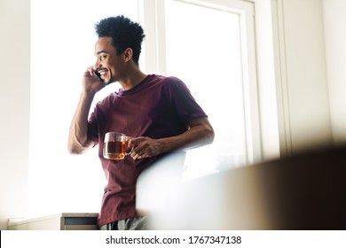 Photo of joyful african american man drinking tea while talking on cellphone in kitchen at home - Powered by Shutterstock