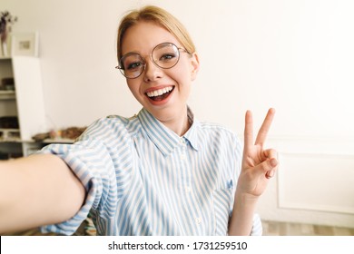 Photo Of Joyful Blonde Woman In Eyeglasses Showing Peace Sign While Taking Selfie Photo At Office