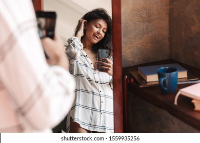 Photo Of Joyful Brunette Woman Wearing Shirt Taking Selfie Photo And Looking At Mirror In Apartment