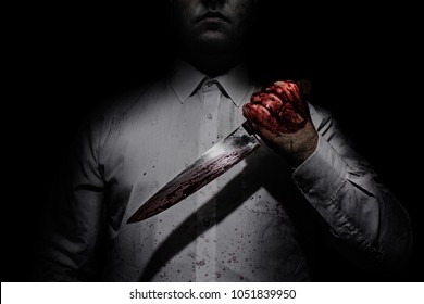 Photo of a killer in white shirt holding a bloody knife on black background with upper lighting.