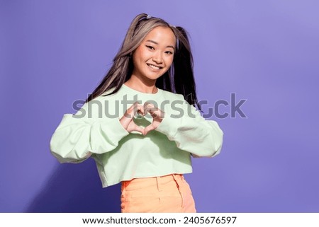 Photo of kind pleasant korean girl with ponytails hairdo wear oversize pullover fingers showing heart isolated on violet color background
