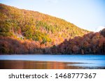 Photo of a lake surrounded with mountains with lots of colorful trees on a sunny afternoon. Beautiful fall foliage. Shot in Mont Saint-Hilaire, Quebec, Canada.