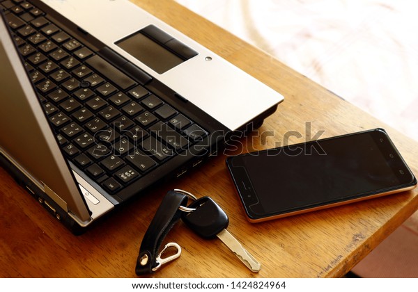 Photo of a laptop computer, car key and\
smartphone on a table inside a\
bedroom