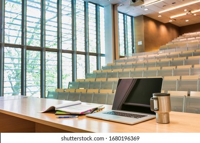 Photo Of Laptop On Professor Desk With Lesson Plan And Tumbler In Empty Classroom Due To Coronavirus