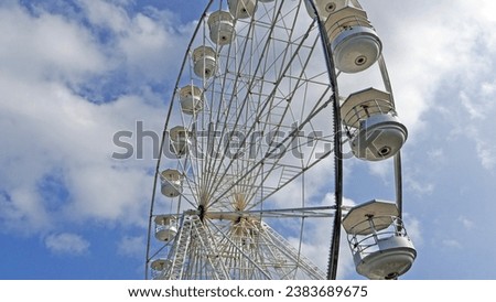 A photo of a large white Ferris Panoramic wheel spinning on a sunny day with a blue sky