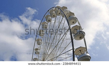 A photo of a large white Ferris Panoramic wheel spinning on a sunny day with a blue sky