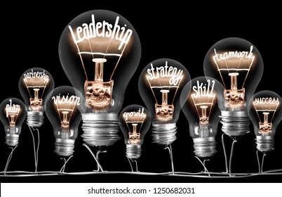 Foto der Gruppe der Glühbirnen mit glänzenden Fasern in Form von mit dem LEADERSHIP-Konzept zusammenhängenden Wörtern einzeln auf schwarzem Hintergrund