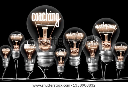 Photo of light bulbs group with shining fibers in a shape of Coaching concept related words isolated on black background