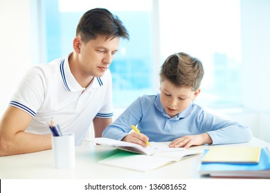 Photo little boy drawing writing in copybook and his father near by