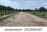 A photo of a long, deserted concrete bridge with weathered railings. The bridge stretches across a rural landscape, with lush green fields and trees visible on both sides