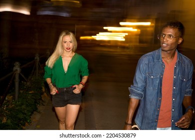 Photo With Long Exposure Of Two Multiethnic People Walking In The Street At Night