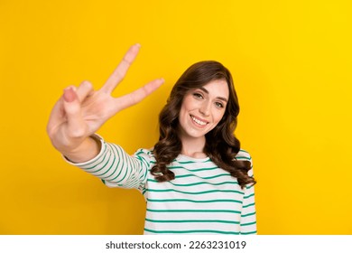 Photo of lovely cheerful girl toothy smile hand fingers demonstrate v-sign isolated on yellow color background