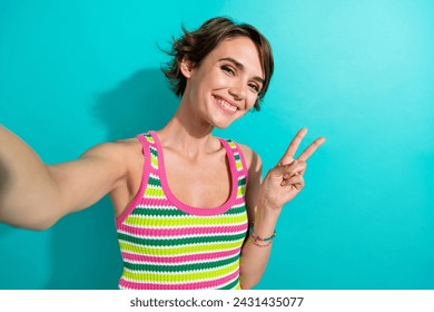 Photo of lovely cheerful girl toothy smile make selfie demonstrate v-sign isolated on teal color background