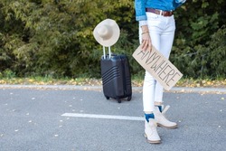 Photo Of Lower Body Of Woman Wait Passing Car In Forest Standing With Suitcase And Cardboard Poster On Roadside. Person Escape From City To Go Anywhere. Travelling, Auto Stop, Hitchhiking, Vacations.