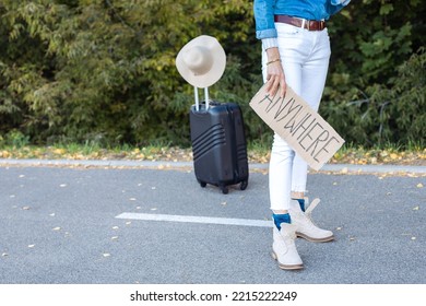 Photo Of Lower Body Of Woman Wait Passing Car In Forest Standing With Suitcase And Cardboard Poster On Roadside. Person Escape From City To Go Anywhere. Travelling, Auto Stop, Hitchhiking, Vacations.