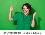 Photo of lucky funny young lady dressed casual t-shirt smiling rising fists isolated green color background