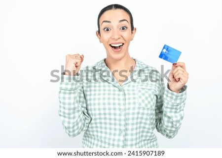 Photo of lucky impressed Beautiful young woman wearing green plaid pyjama arm fist holding credit card. Celebrated