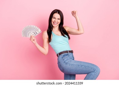 Photo of lucky millennial lady hold money hand fist wear blue top jeans isolated on pink background
