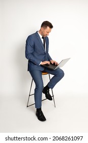 Photo Of Man 40 Years Old Sits On Bar Stool On White Background In Studio. Lap Top On Knees, Works, Looks Into Frame, Manager Posing Tiping On Laptop